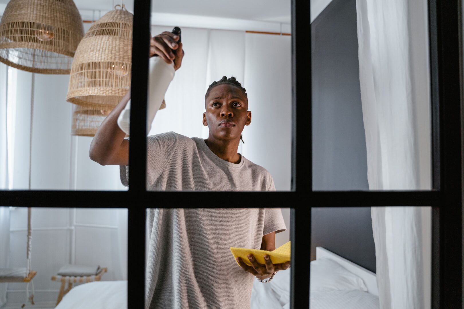 Man cleaning glass window indoors using a spray bottle and cloth.